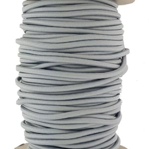 May include: A spool of grey elastic cord. The cord is wound tightly around a cardboard spool.