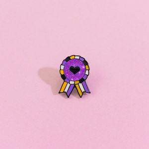 May include: Purple, yellow, and black glitter enamel pin with a black heart in the center. The pin is shaped like a ribbon.