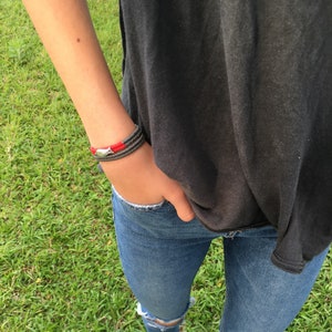 May include: A person wearing a black t-shirt, blue jeans with rips, and white sneakers. They are wearing a red and gray bracelet on their wrist.