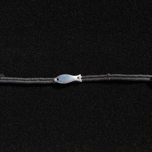 以下が含まれることがあります： 黒いコードのブレスレットに、銀色の魚のチャームと銀色のボタンが付いている