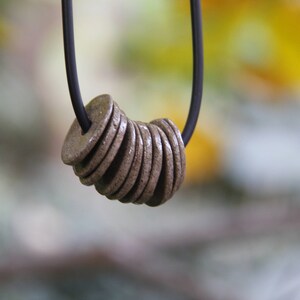 May include: A necklace with a black cord and a pendant made of stacked, round, brown ceramic discs.