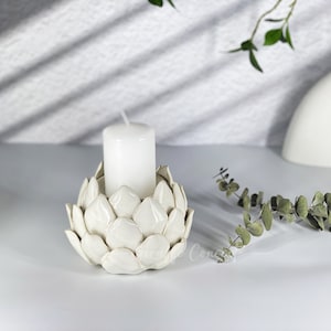 May include: White ceramic candle holder shaped like an artichoke with a white candle inside.