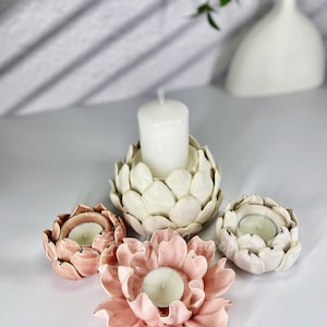 May include: Four ceramic candle holders in the shape of flowers. Two are white and two are pink. The white candle holders have a textured surface that resembles a flower bud. The pink candle holders have a smooth surface and resemble a flower in full bloom. Each candle holder has a small opening in the center for a tea light candle.
