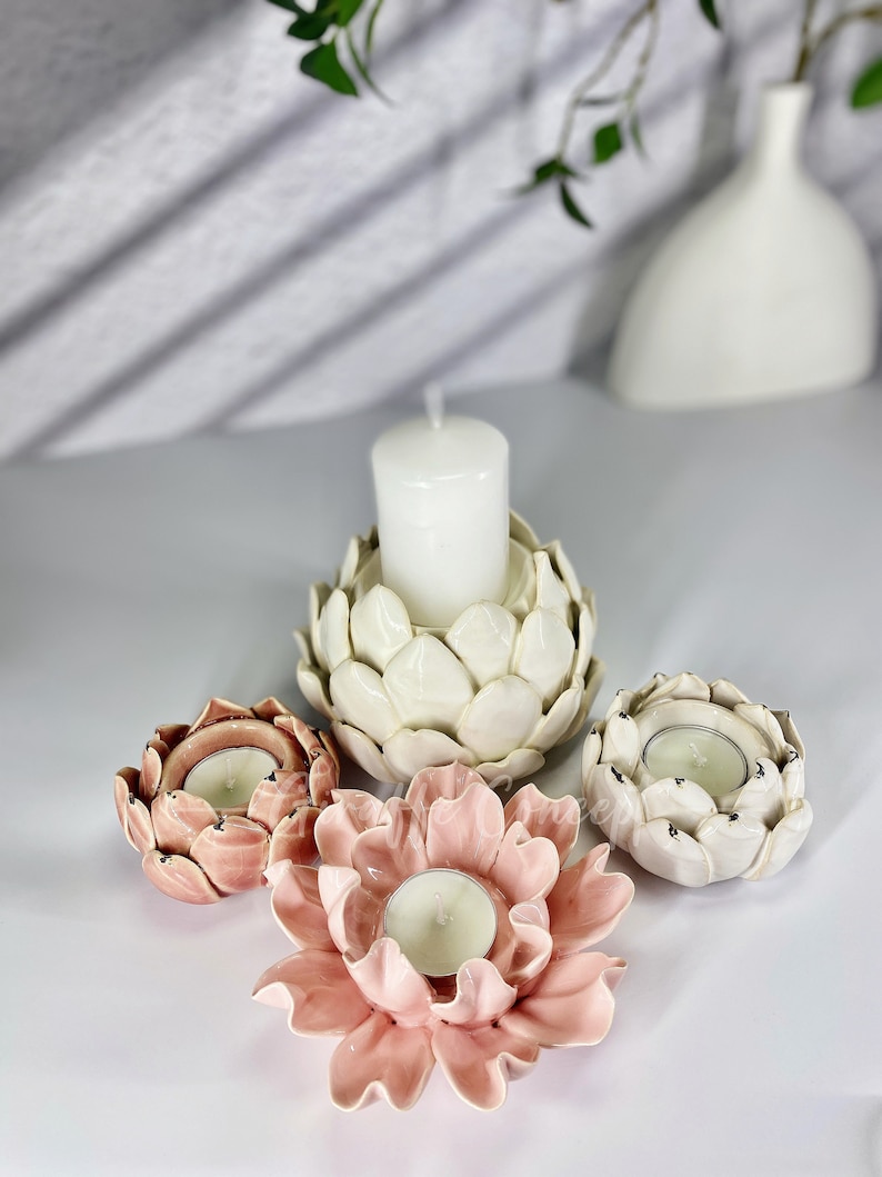 May include: Four ceramic candle holders in the shape of flowers. Two are white and two are pink. The white candle holders have a textured surface that resembles a flower bud. The pink candle holders have a smooth surface and resemble a flower in full bloom. Each candle holder has a small opening in the center for a tea light candle.