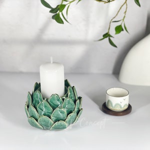 May include: A green ceramic candle holder shaped like a flower with a white candle in the center.