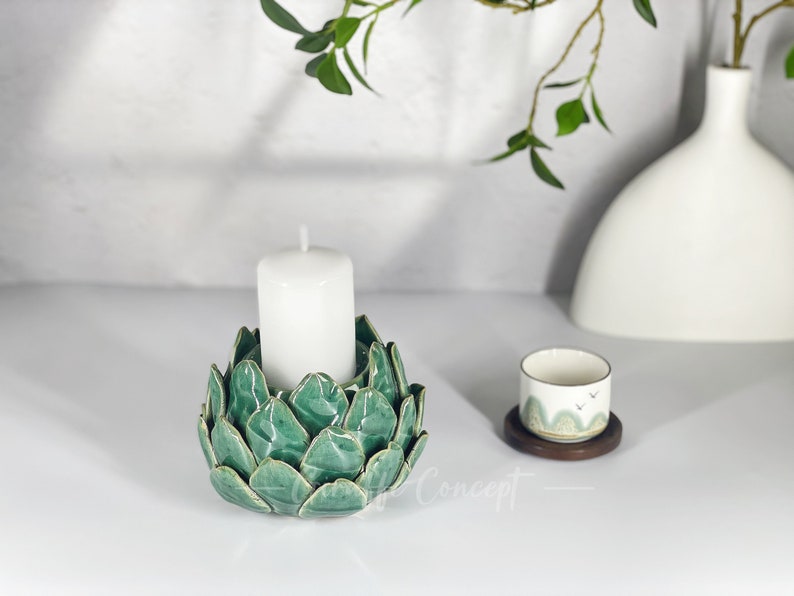 May include: A green ceramic candle holder shaped like a flower with a white candle in the center.