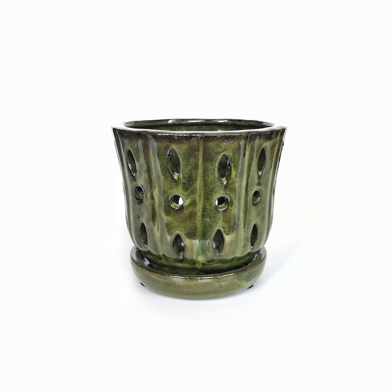 May include: A green ceramic planter with a decorative, openwork design and a matching saucer. The planter has a rounded shape and a slightly flared rim.