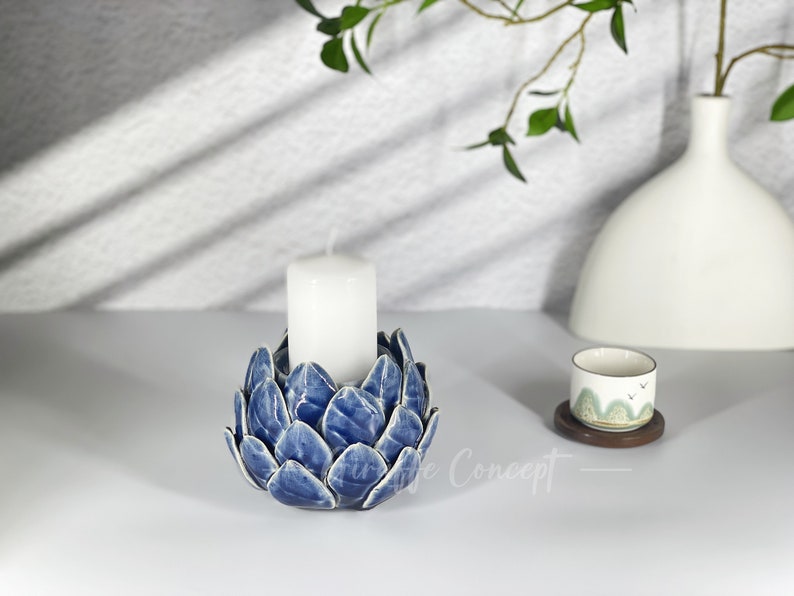 May include: Blue ceramic candle holder shaped like an artichoke with a white candle inside.