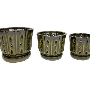 May include: Set of three green ceramic planter pots with drainage holes and matching saucers. The pots have a textured, ribbed design.