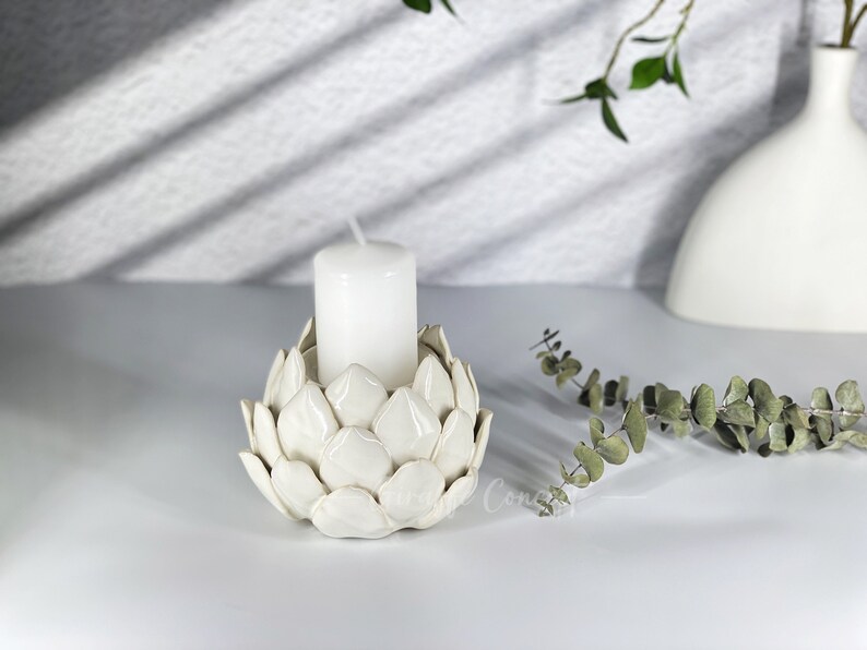 May include: White ceramic candle holder shaped like an artichoke with a white candle inside.