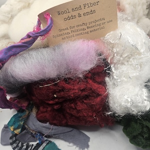 May include: A pile of wool and fiber odds and ends in various colors, including white, pink, red, black, and green. The pile is labeled "Wool and Fiber odds & ends" and states "Great for crafty projects; Spinning, Felting, Weaving or use as bird nesting material."