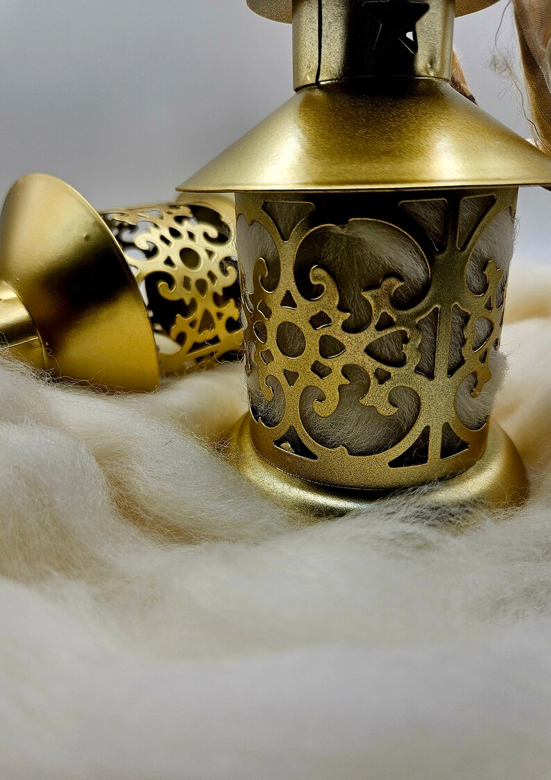 May include: Two gold metal lanterns with intricate cut-out designs. The lanterns are sitting on a white fluffy surface.