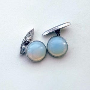 May include: A pair of silver cufflinks with round, iridescent white opal stones.