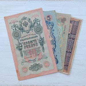 Op de afbeelding: Een verzameling van vier vintage Russische bankbiljetten, waaiervormig gerangschikt. Het voorste biljet is een biljet van 10 roebel uit 1909, voorzien van ingewikkeld krulwerk, een tweekoppig adelaars-embleem en tekst in het Cyrillisch.