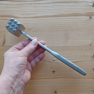 May include: A silver meat tenderiser with a long handle. The tenderiser has a square head with a pattern of small, raised triangles.