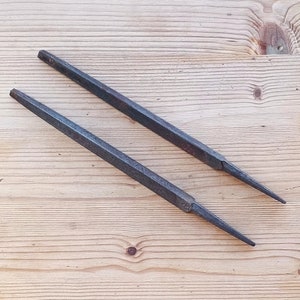 Puede incluir: Dos limas de metal con un acabado ligeramente oxidado. Las limas están dispuestas sobre una superficie de madera clara.