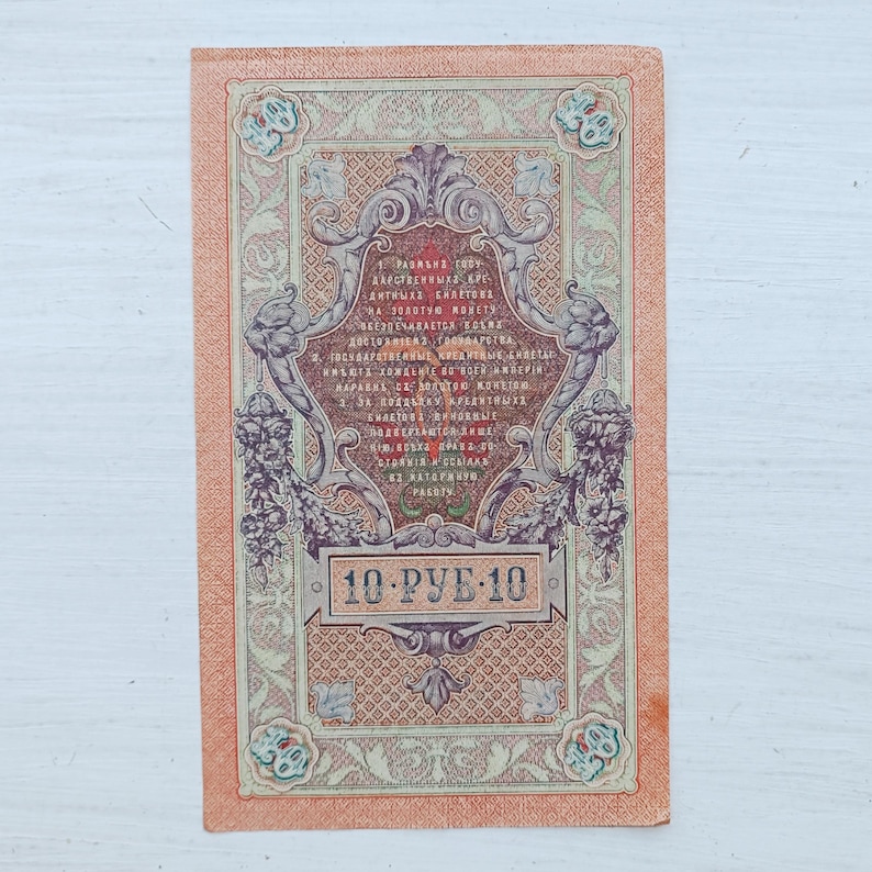 Op de afbeelding: Een rechthoekig vintage Russisch bankbiljet van 10 roebel met ingewikkelde ornamenten, bloemmotieven en cyrillische tekst in zwarte en rode inkt op een perzikkleurige achtergrond, met het getal 10 weergegeven in de hoeken van het biljet.