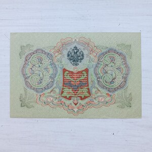 Op de afbeelding: Een vintage Russisch bankbiljet van drie roebel met een ingewikkeld guillochepatroon in groen, rood en blauw. Het ontwerp bevat een centraal embleem met een tweekoppige adelaar, grote cijfers drie aan beide kanten en cyrillische tekst in een rood schild.