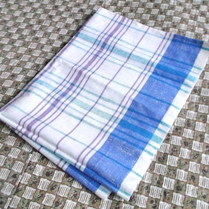 May include: A rectangular kitchen towel featuring a white base with a plaid pattern in shades of purple, light blue, and dark blue. The fabric displays a prominent wide blue border on one side, complemented by thinner intersecting lines throughout.