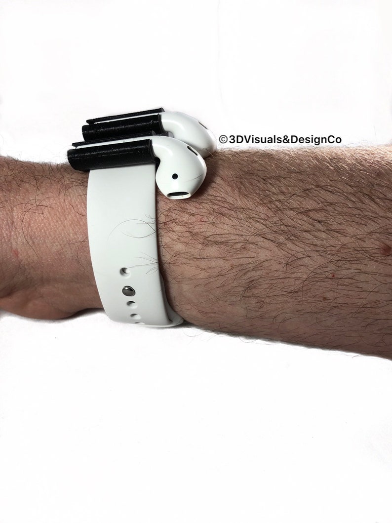 K&ouml;nnte beinhalten: Ein wei&szlig;es Armband mit einem schwarzen 3D-gedruckten Aufsatz zum Halten von drahtlosen Ohrh&ouml;rern. Der Text "&copy;3DVisuals&DesignCo" ist im Bild sichtbar.