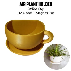 May include: A gold-colored ceramic coffee cup with a saucer, designed to hold an air plant. The cup has a handle and is shaped like a traditional coffee cup. The image also shows a white ceramic cup with a saucer holding an air plant, mounted on a wall.