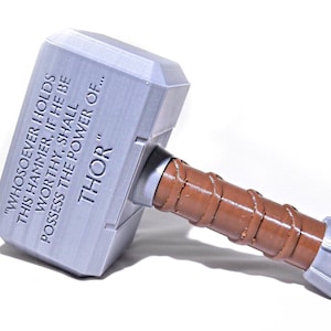 May include: A silver-colored replica of Thor's hammer, Mjolnir, with a brown leather handle. The hammer has an inscription that reads "Whosoever holds this hammer, if he be worthy, shall possess the power of... THOR"