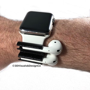 K&ouml;nnte beinhalten: Eine wei&szlig;e Apple Watch mit einem schwarzen Armband und einem schwarzen 3D-gedruckten Halter f&uuml;r wei&szlig;e kabellose Ohrh&ouml;rer. Der Halter ist am Armband der Uhr befestigt.