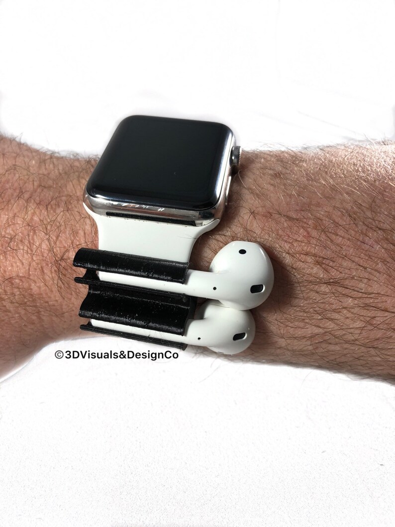 K&ouml;nnte beinhalten: Eine wei&szlig;e Apple Watch mit einem schwarzen Armband und einem schwarzen 3D-gedruckten Halter f&uuml;r wei&szlig;e kabellose Ohrh&ouml;rer. Der Halter ist am Armband der Uhr befestigt.