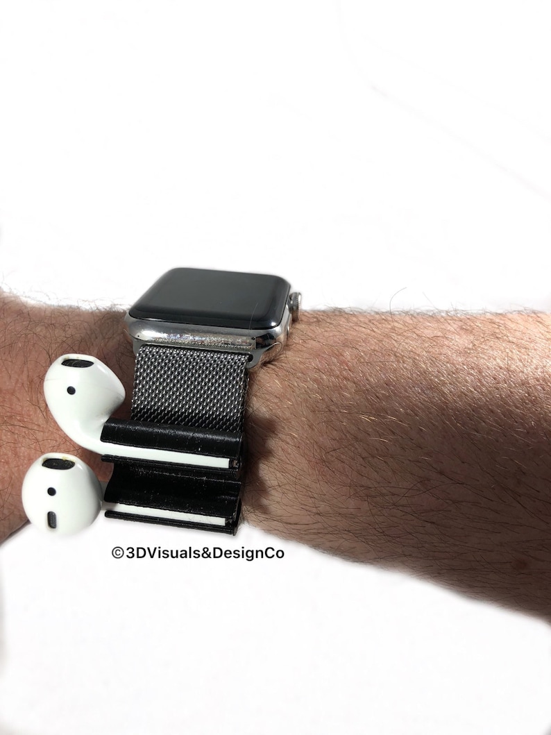 K&ouml;nnte beinhalten: Ein schwarz-wei&szlig;es 3D-gedrucktes Zubeh&ouml;r f&uuml;r eine Smartwatch, das zum Halten von kabellosen Ohrh&ouml;rern entwickelt wurde. Das Zubeh&ouml;r ist an einem silbernen Smartwatch-Armband mit einem schwarzen Mesh-Armband befestigt. Der Text "&copy;3DVisuals&DesignCo" ist im Bild sichtbar.