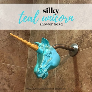 May include: Teal blue unicorn shower head with a gold horn. The shower head is mounted on a silver shower arm. The text "silky teal unicorn shower head" is at the top of the image. The text "www.3Dvisualsandesignco.etsy.co" is at the bottom of the image.