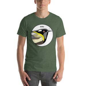 May include: A green t-shirt featuring a white circle with a colourful illustration of a bird, labelled "Hihi" above it.
