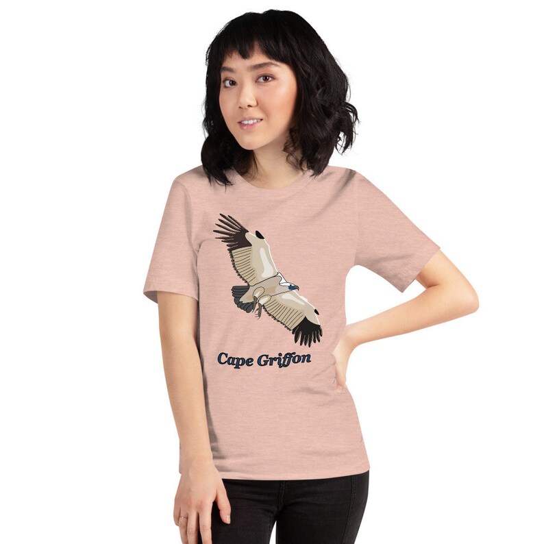 May include: A pink heather t-shirt featuring a graphic of a Cape Griffon in flight. The text "Cape Griffon" is printed in blue below the bird.