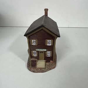 May include: A miniature brown ceramic house with a dark brown roof and a brick chimney. The house has white-framed windows and a door. The text "NICOLSON STORE" is printed on the front of the house.
