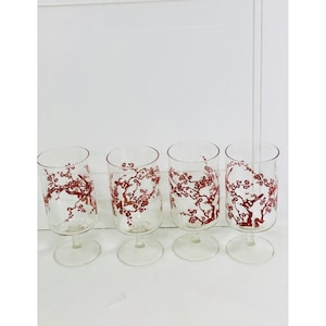 Puede incluir: Cuatro copas transparentes con un estampado floral rojo. Las copas están dispuestas en fila sobre un fondo blanco. El diseño floral parece ser flores de cerezo.