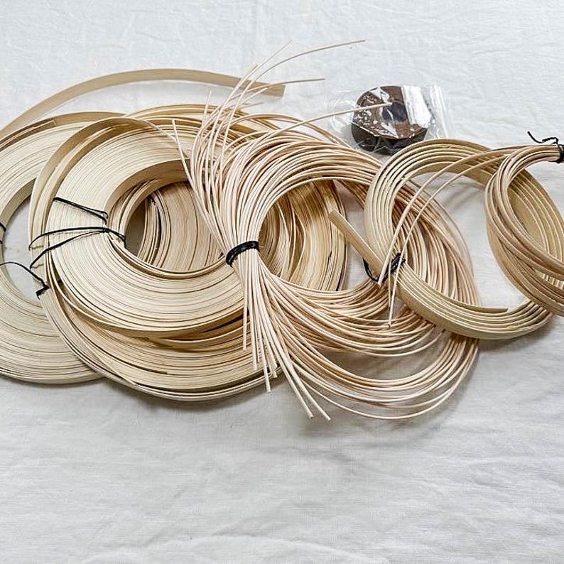 May include: Several coils of natural-coloured rattan strips and bundles of thin, straight rattan pieces. The coils are bound with black twine. A small, clear plastic bag with a dark object is also visible.