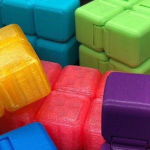 May include: A collection of colourful, multi-sided, fidget toys made of plastic. The toys are in various shades of blue, green, yellow, red, and purple.