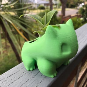 May include: A green 3D printed planter shaped like a cartoon character with a small plant growing inside.