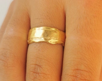 May include: A gold band ring with a textured, irregular surface. The ring is worn on a finger.