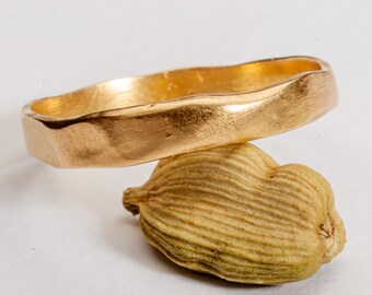 May include: A gold ring with a textured, hammered finish. The ring is thick and has a rounded shape.