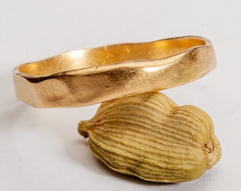 May include: A gold ring with a textured, hammered finish. The ring is thick and has a rounded shape.