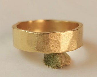 May include: A gold-coloured ring with a textured, hammered finish. The ring is thick and has a wide band.