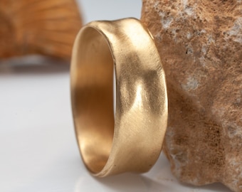 May include: A gold-colored ring with a textured, hammered finish. The ring is thick and has a wide band.