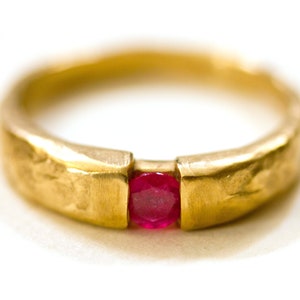 May include: A gold ring with a textured band and a single red ruby gemstone set in the center.