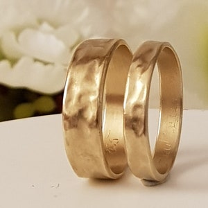 May include: Two gold wedding bands with a hammered texture. The bands are stacked on top of each other.