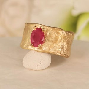 May include: A gold ring with a textured band and a red oval gemstone.