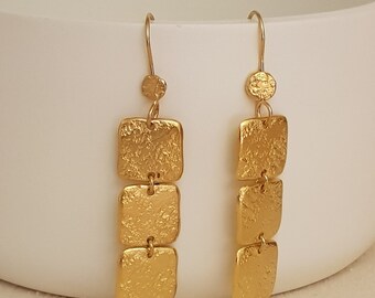 May include: Gold dangle earrings with three square-shaped charms. Each charm has a textured surface.