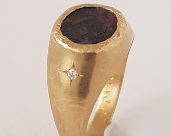 May include: A gold signet ring with a dark red stone set in the center. The ring has a single diamond set in a star shape on the side.