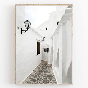May include: A narrow, white-washed alleyway with a cobblestone floor.  The walls are lined with traditional lanterns and the alleyway leads to a bright, open space.