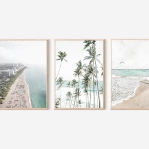 Pode incluir: Conjunto de tr&ecirc;s impress&otilde;es de praia emolduradas. A primeira mostra uma vista a&eacute;rea costeira com edif&iacute;cios e uma praia. A segunda apresenta palmeiras. A terceira mostra ondas numa praia arenosa com p&aacute;ssaros no c&eacute;u.