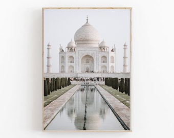 May include: A white marble building with a large dome and minarets, reflected in a long pool of water. The building is surrounded by green trees and a crowd of people can be seen in the distance.